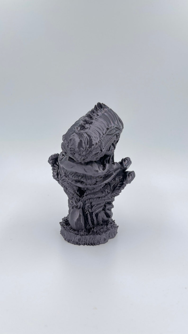 May include: A 3D printed figurine of a creature with a large head and a body that resembles a twisted, gnarled tree. The creature is painted in a dark gray color.