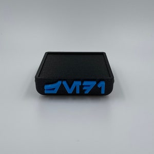 May include: A black square-shaped coaster with the text "VT71" in blue lettering.