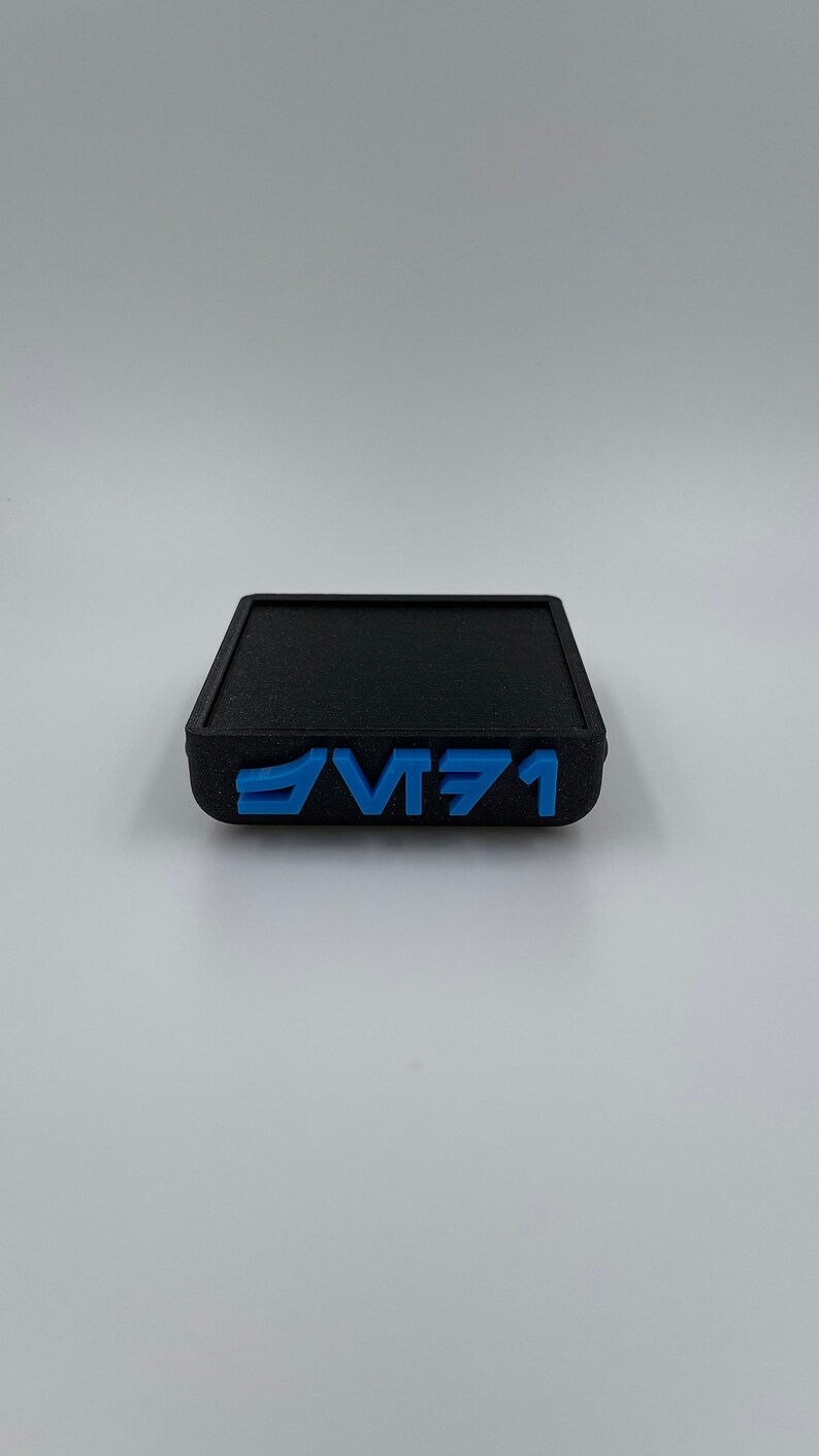 May include: A black square-shaped coaster with the text "VT71" in blue lettering.