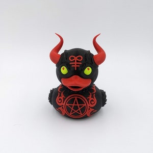 May include: A black rubber duck with red horns and a pentagram on its chest. The duck has yellow eyes and a red beak.