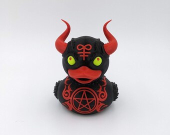 May include: A black rubber duck with red horns and a pentagram on its chest. The duck has yellow eyes and a red beak.