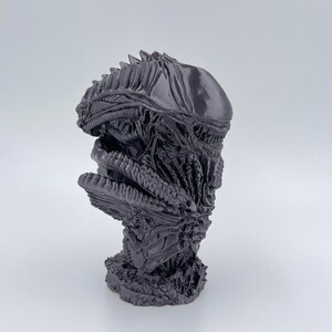 May include: A 3D printed bust of an alien creature with a detailed, textured surface. The bust is painted in a dark gray color.