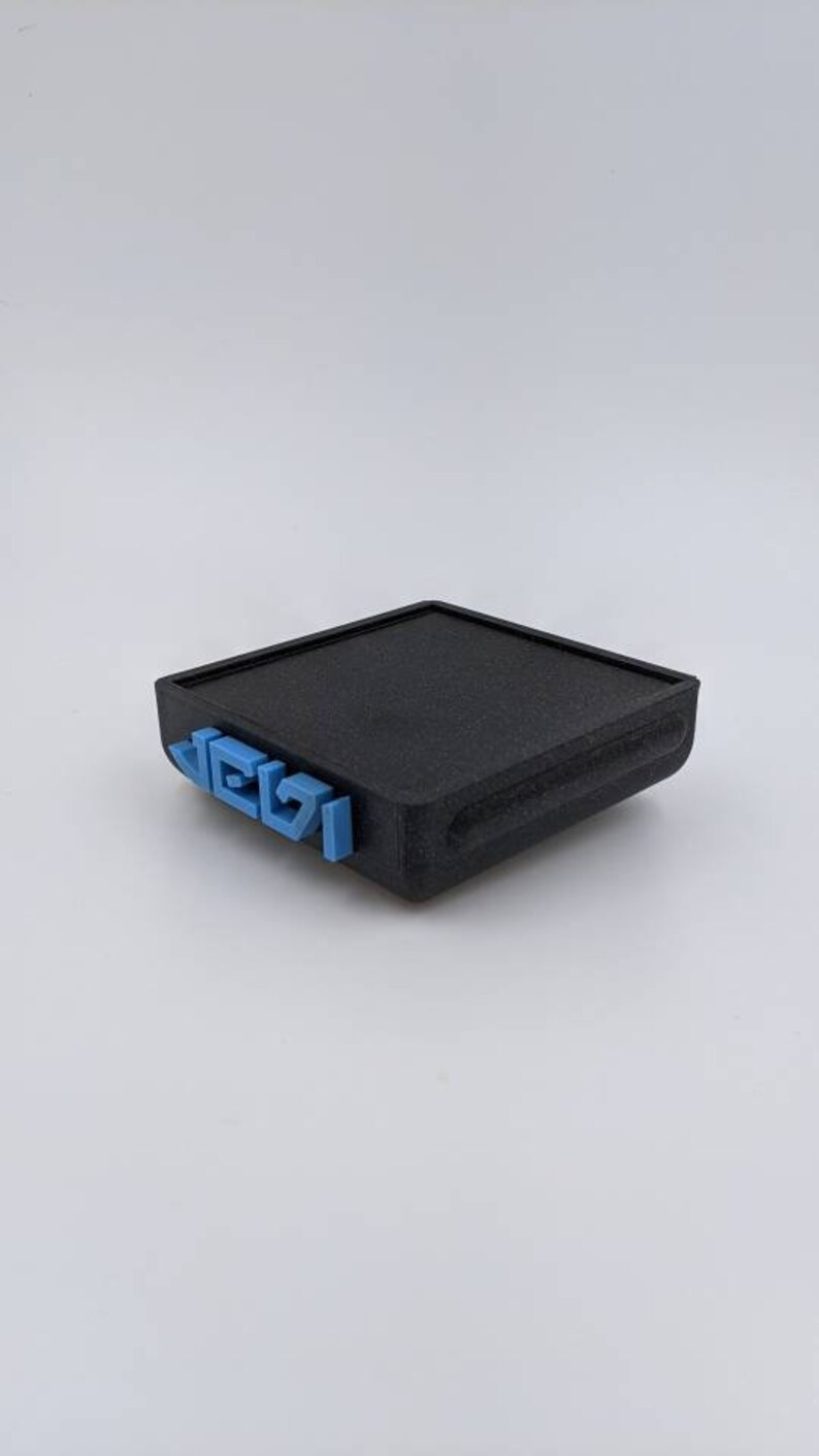 May include: A black rectangular box with a textured surface. The box has a blue inscription on the front that reads "LEGO".