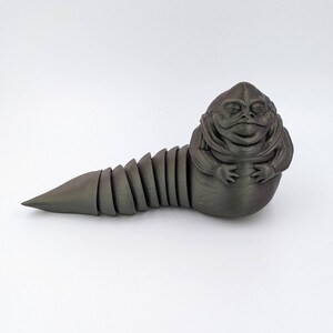 Puede incluir: Una figura de Jabba el Hutt de Star Wars impresa en 3D de color gris oscuro. La figura est&aacute; en posici&oacute;n enroscada con una cola segmentada.