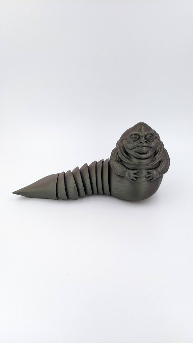 Puede incluir: Una figura de Jabba el Hutt de Star Wars impresa en 3D de color gris oscuro. La figura est&aacute; en posici&oacute;n enroscada con una cola segmentada.