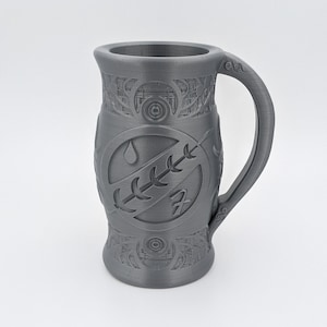 May include: A gray ceramic mug with a detailed design featuring a stylized symbol of a water drop and a plant. The mug has a handle and a textured surface.