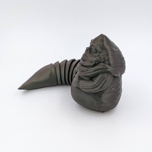 Puede incluir: Una figura de pl&aacute;stico gris oscuro impresa en 3D de una criatura del universo de Star Wars. La criatura tiene un cuerpo grande y redondo con una cola larga y delgada. La cabeza de la criatura es peque&ntilde;a y tiene una boca grande y redonda.