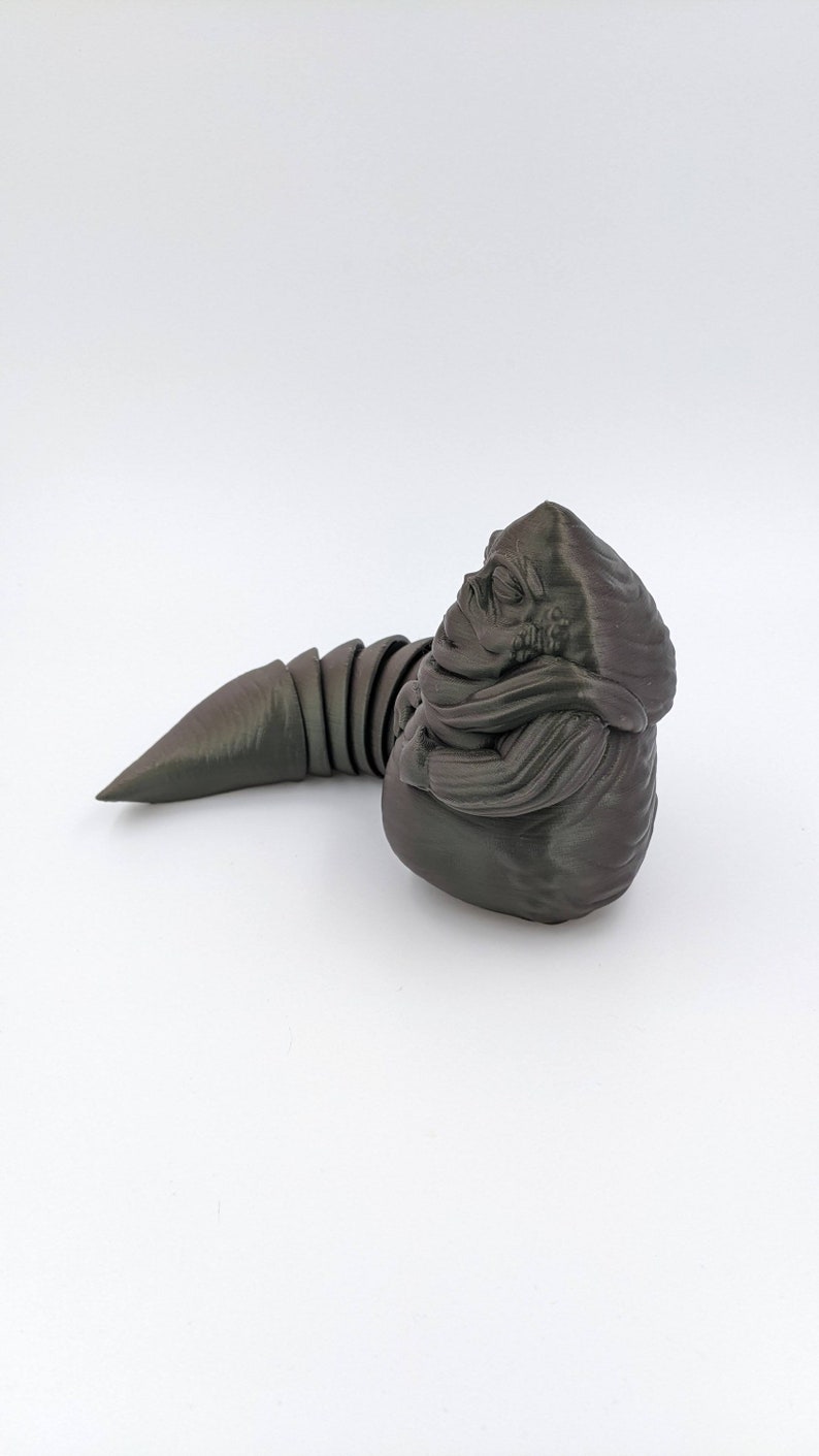 Puede incluir: Una figura de pl&aacute;stico gris oscuro impresa en 3D de una criatura del universo de Star Wars. La criatura tiene un cuerpo grande y redondo con una cola larga y delgada. La cabeza de la criatura es peque&ntilde;a y tiene una boca grande y redonda.