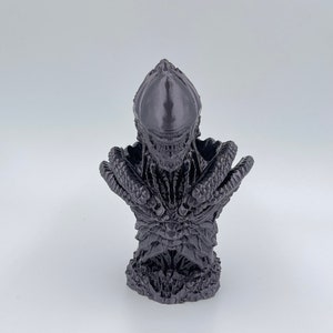 May include: A dark gray 3D printed bust of a creature with a large head and sharp teeth. The creature has a textured, scaly body and appears to be from a science fiction or fantasy movie.