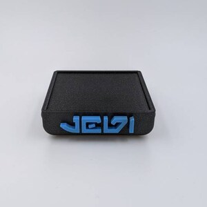 May include: A black square-shaped box with the word "JELZI" printed in blue on the front.