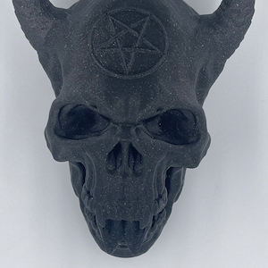 May include: Black skull with horns and a pentagram on the forehead. The skull has a detailed design and appears to be made of a textured material.