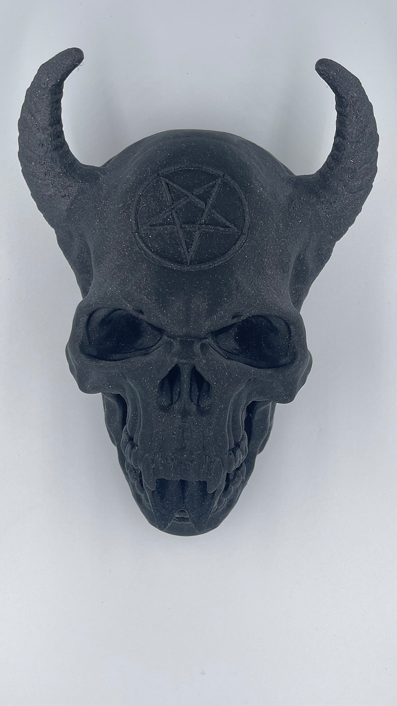 May include: Black skull with horns and a pentagram on the forehead. The skull has a detailed design and appears to be made of a textured material.