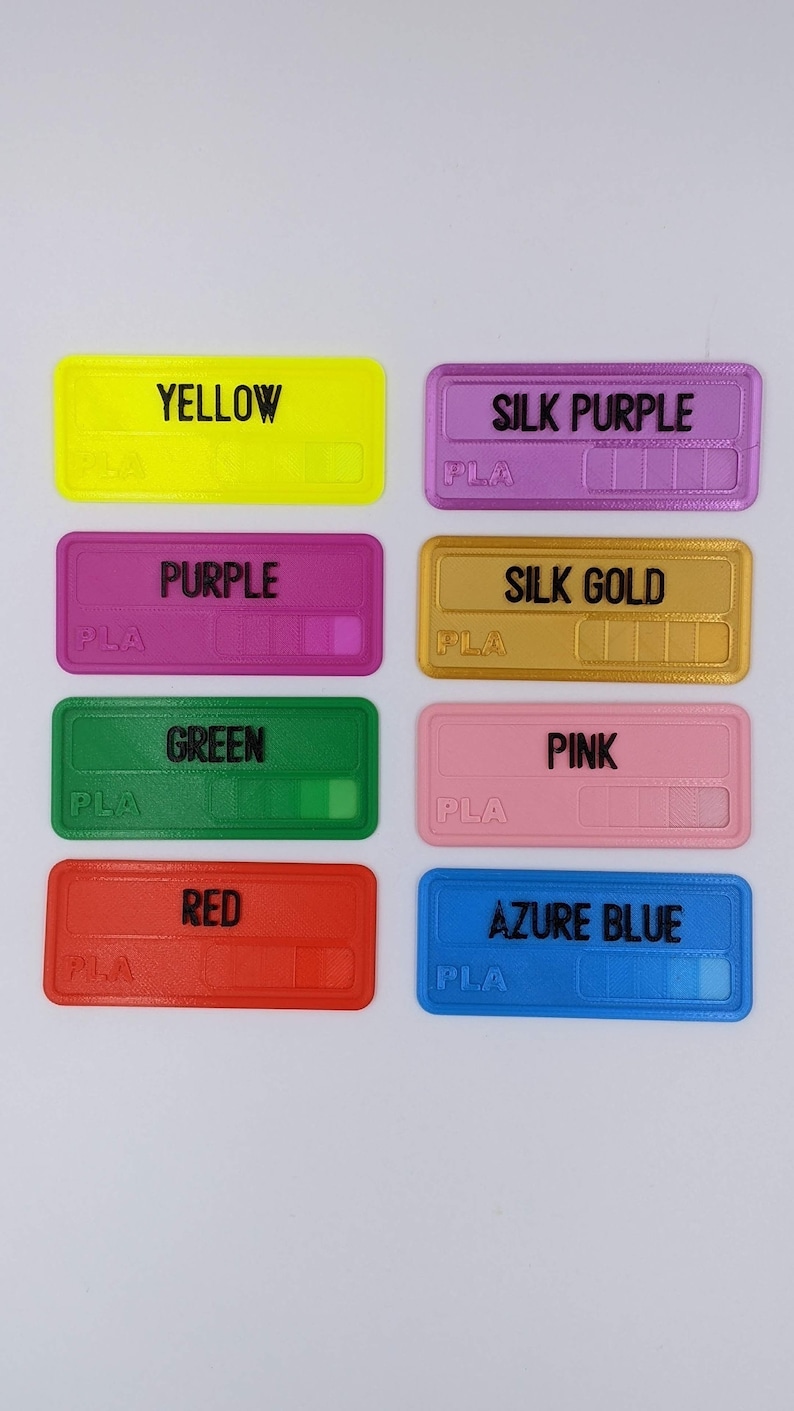May include: Eight sample filament spools labelled with their colours and material type: yellow, silk purple, purple, silk gold, green, pink, red, and azure blue. Each spool is labelled "PLA".