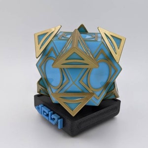 May include: A blue and gold geometric sculpture with a black base. The base has the word "DELZI" printed on it in blue.