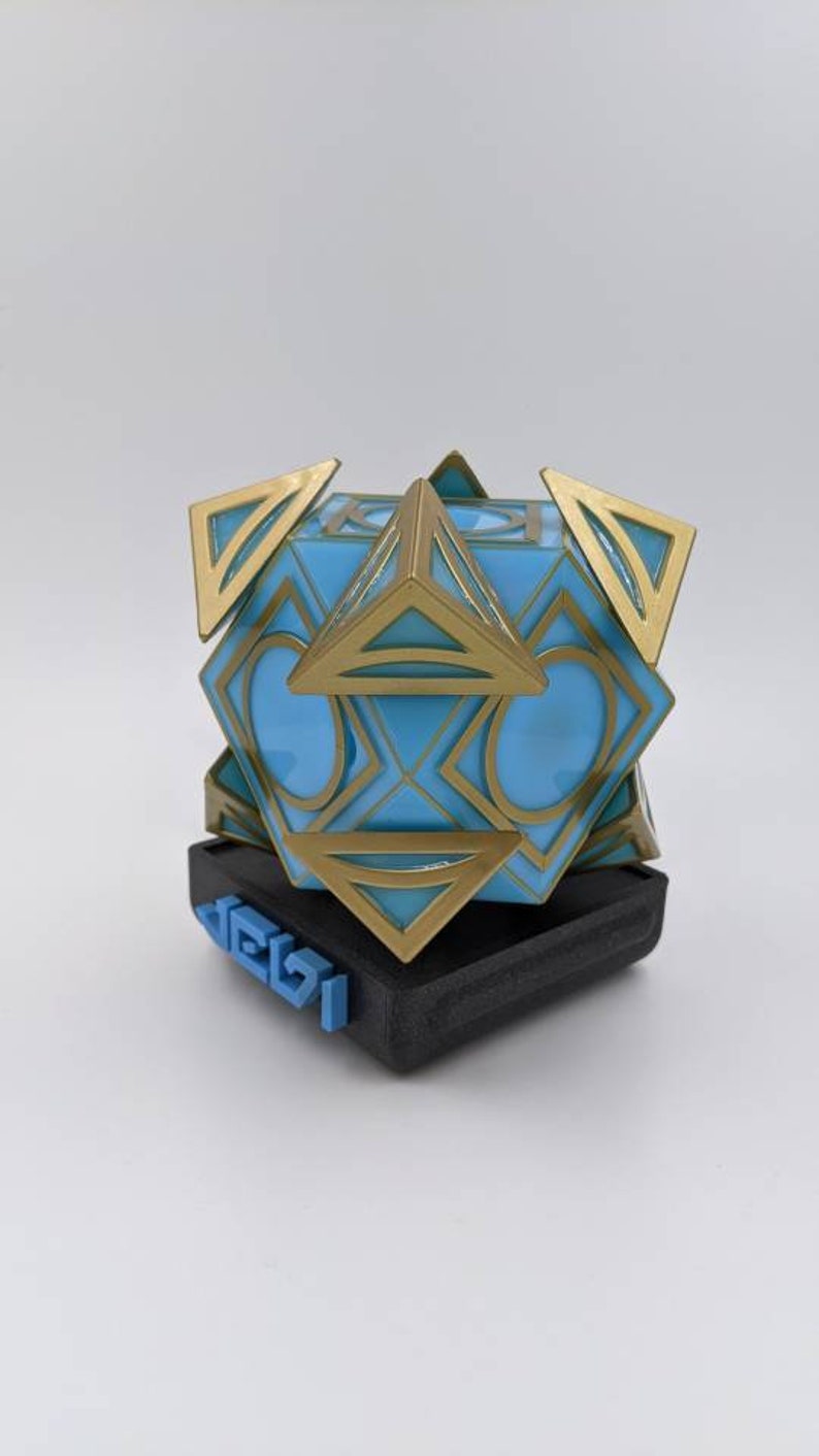 May include: A blue and gold geometric sculpture with a black base. The base has the word "DELZI" printed on it in blue.
