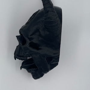 May include: A black 3D printed skull with horns. The skull is detailed with a textured surface and open mouth.