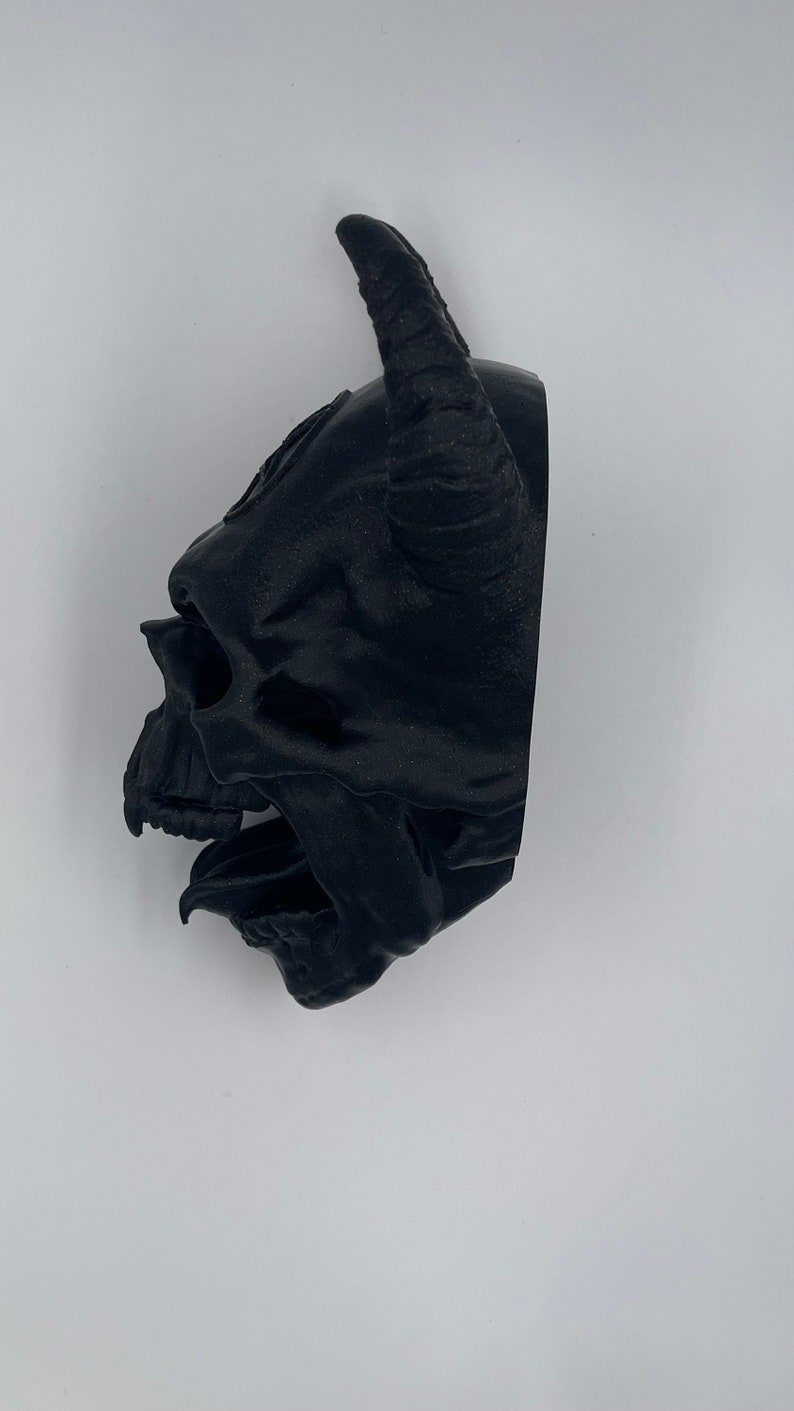 May include: A black 3D printed skull with horns. The skull is detailed with a textured surface and open mouth.