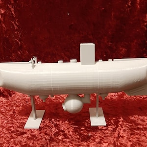 Peut inclure: Modèle d'un sous-marin imprimé en 3D en blanc sur un support blanc. Le sous-marin a un corps arrondi et une petite tour sur le dessus.