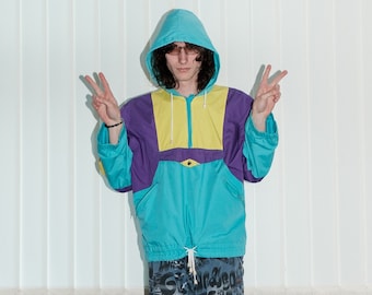 May include: A person wearing a turquoise, purple, and yellow hooded jacket with a zipper and a drawstring. They are also wearing blue and white patterned shorts and black and white shoes.