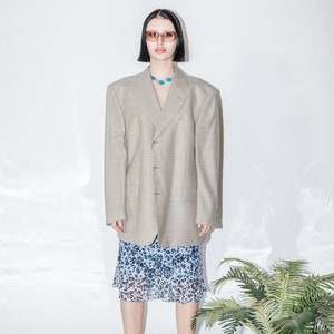May include: A woman wearing a light gray blazer with a blue and white patterned skirt and pink shoes. She is wearing a turquoise necklace and sunglasses.