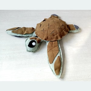 Könnte beinhalten: Ein braunes und grünes Plüsch-Schildkrötenspielzeug mit einem segmentierten Panzer und schwarzen Augen.