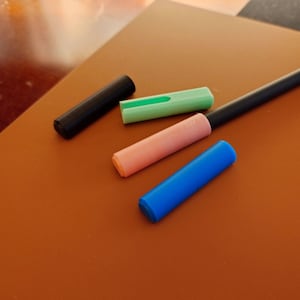 May include: Four different coloured pen caps, including black, green, pink, and blue. The caps are made of plastic and are designed to fit over the ends of pens.