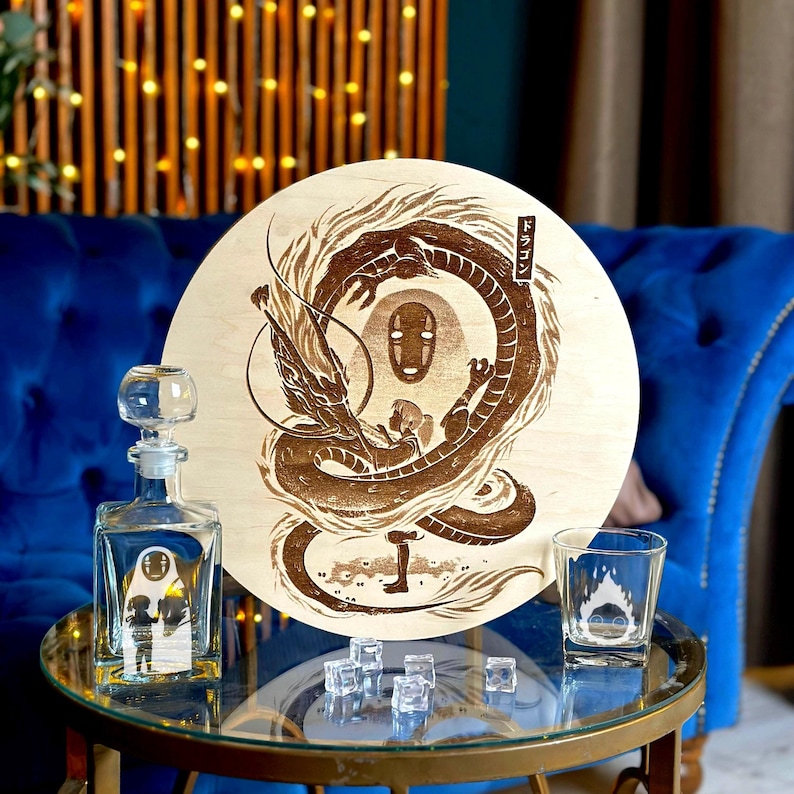 May include: A wooden round sign with a dragon illustration and Japanese text. A glass decanter and shot glass with matching artwork sit on a glass table. Clear ice cubes are scattered on the table.