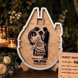 May include: A wooden guest book frame shaped like a spaceship, featuring a laser-cut silhouette of two figures, the text I love you I know, and the names Ashley & Wilson with the date 15 March 2025. A small wooden sign with instructions is included.