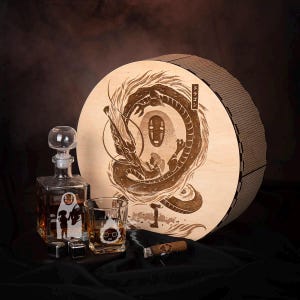 May include: A wooden round box with a dragon and character design, a glass decanter, a rocks glass, and a cigar. The decanter and rocks glass have character designs. The box is round with a brown finish.