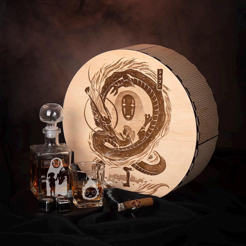May include: A wooden round box with a dragon and character design, a glass decanter, a rocks glass, and a cigar. The decanter and rocks glass have character designs. The box is round with a brown finish.