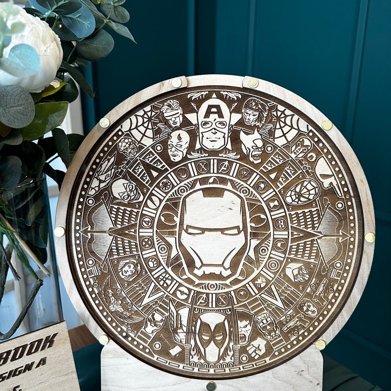 May include: A wooden round wall clock with a detailed design featuring a compass, stars, and various superhero characters. The clock face is surrounded by a ring of superhero characters, including Captain America, Iron Man, and Thor. The clock is made of wood and has a brown finish.