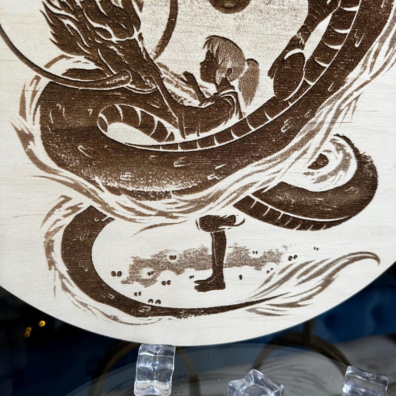 May include: A wooden art piece featuring a dragon and a girl. The dragon is intricately carved in brown, wrapping around the girl. The girl is in silhouette, with her hands raised. The background is light-colored wood.