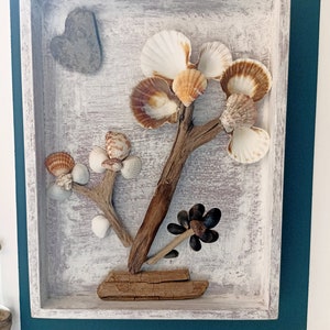 Peut inclure: Un cadre en bois blanc avec une œuvre d'art en coquillages à l'intérieur. Les coquillages sont disposés pour ressembler à un arbre avec une pierre en forme de cœur au sommet.