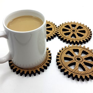Pode incluir: Quatro  tábuas de madeira em forma de engrenagens, com uma caneca branca em cima de uma das tábuas. A caneca está cheia de uma bebida marrom clara.
