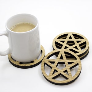 Pode incluir: Conjunto de quatro  tábuas de madeira com um design de estrela de cinco pontas. As tábuas são de cor castanho com um contorno preto e estão empilhadas umas sobre as outras. Uma caneca de café branca está sentada em uma das tábuas.