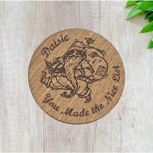 Könnte beinhalten: Ein runder Holzanhänger mit einem lasergravierten Bild vom Weihnachtsmann, der einen Sack mit Geschenken trägt. Der Anhänger trägt die Aufschrift "Daisie You Made the Nice List".