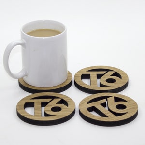 Può includere: Quattro sottobicchieri rotondi in legno con bordo nero e il numero "76" tagliato al centro. Una tazza bianca con un liquido marrone si trova su uno dei sottobicchieri.