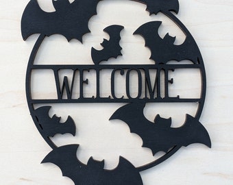 May include: Black wooden welcome sign with a circle design and bats surrounding the word "WELCOME".