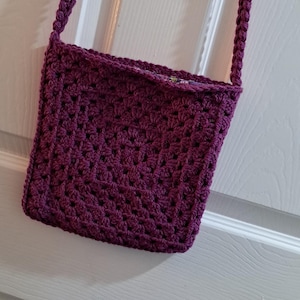 Può includere: Una piccola borsa a tracolla in crochet viola con un cinturino lungo.