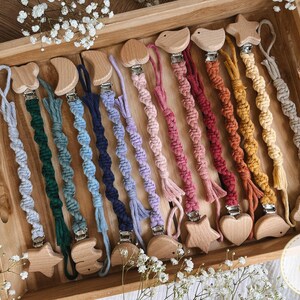 May include: A collection of 14 colorful crocheted baby teethers with wooden attachments in various shapes, including stars, hearts, and moons. The teethers are displayed on a wooden surface.