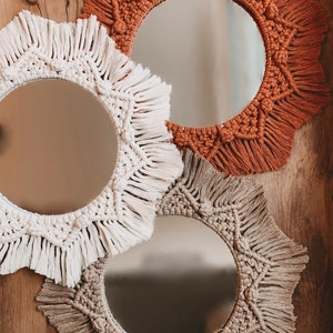 May include: Three round mirrors with macrame frames in beige, white, and brown. The mirrors are hanging on a wooden wall.
