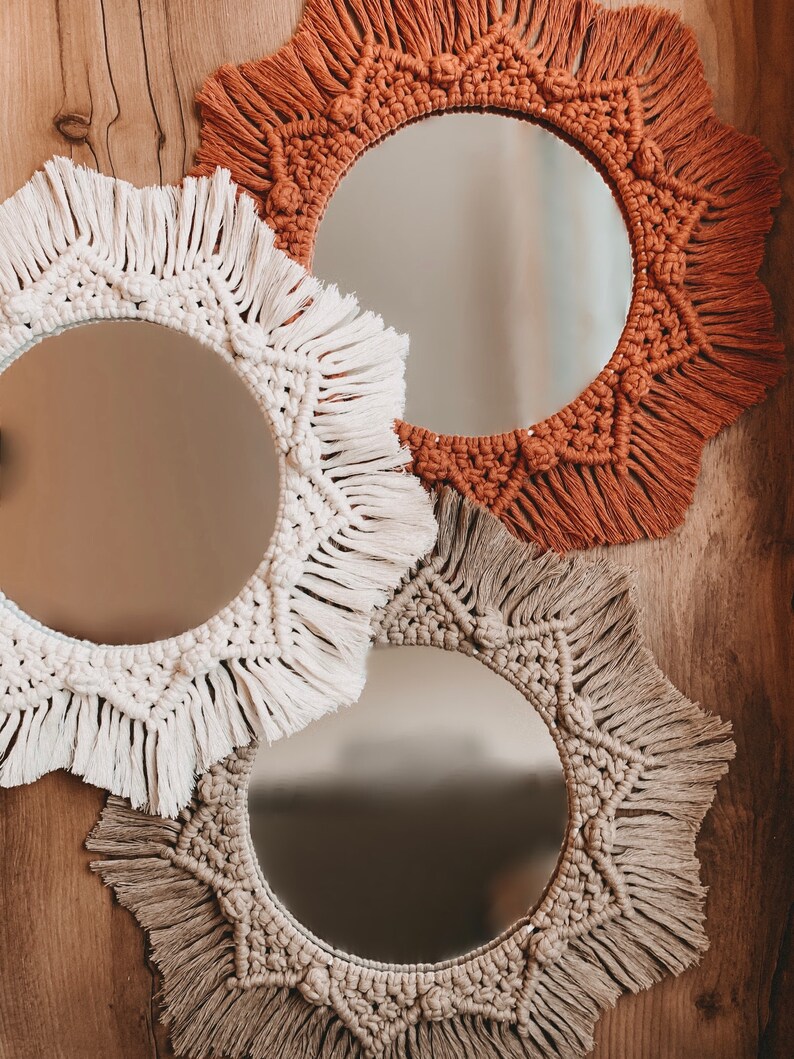 May include: Three round mirrors with macrame frames in beige, white, and brown. The mirrors are hanging on a wooden wall.