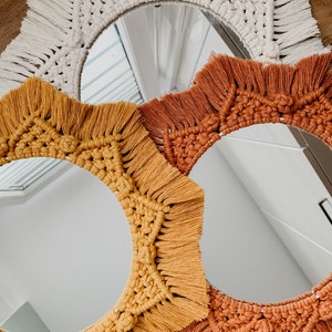 May include: Three round mirrors with macrame frames in white, orange, and yellow. The mirrors are nested inside each other, with the white mirror on top and the yellow mirror on the bottom.