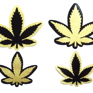 Puede incluir: Cuatro parches decorativos con forma de hoja. Cada parche presenta un diseño de hoja de cannabis negra con un fondo texturizado de color dorado. Los parches están dispuestos sobre un fondo blanco.