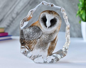 May include: A glass sculpture of a barn owl with brown and white feathers. The owl is perched on a clear glass base with a rough, textured surface. The sculpture is made by the company "SPR"