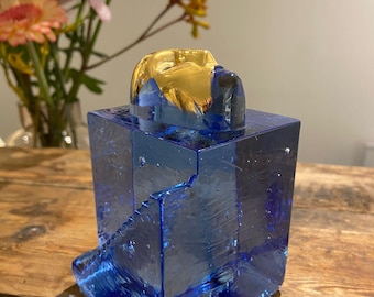 May include: A blue glass sculpture with a gold-leafed top. The sculpture is abstract and has a geometric shape.