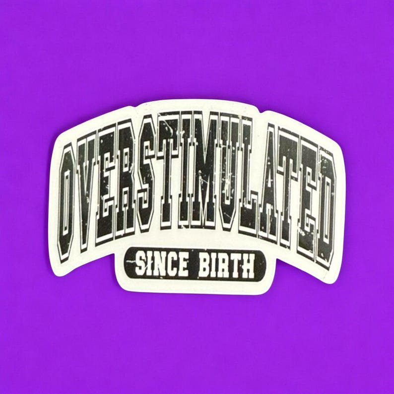 May include: A white sticker with the words "OVERSTIMULATED" in a bold, distressed font, arched across the top. Below, the text "SINCE BIRTH" is centered. The sticker is set against a vibrant purple background.