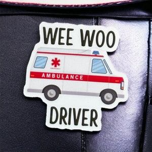 Op de afbeelding: Witte ambulance sticker met rode streep en de woorden "WEE WOO DRIVER" op een zwarte achtergrond.