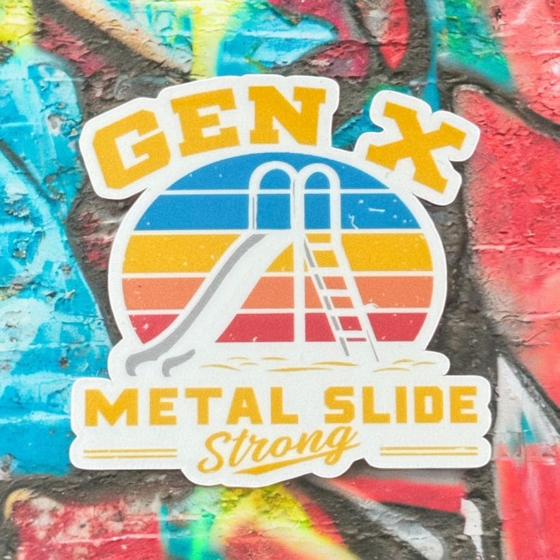 Op de afbeelding: Een sticker met een retro-ontwerp met een metalen glijbaan en de tekst "GEN X METAL SLIDE STRONG". Het ontwerp bevat een kleurrijke zonsondergang met blauwe, gele, oranje en rode strepen. De sticker bevindt zich op een met graffiti bedekte bakstenen muur.