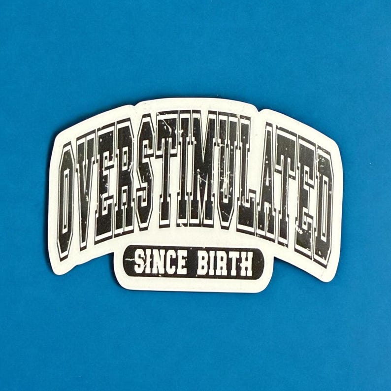 May include: A white sticker with the words "OVERSTIMULATED" in a bold, black, distressed font. Below, in a smaller font, it reads "SINCE BIRTH". The sticker has a curved shape and is set against a blue background.